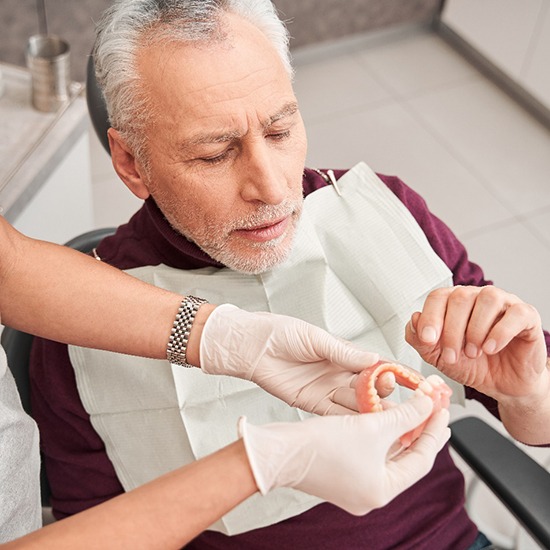 A man in a maroon shirt being handed dentures by a dentist in white gloves