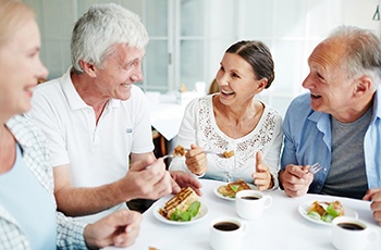 Group of 4 older adults enjoying dessert and coffee at a white table