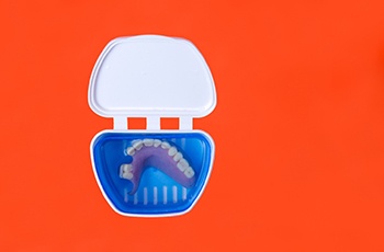 Bird’s eye view of partial dentures in a container with clear liquid over an orange background