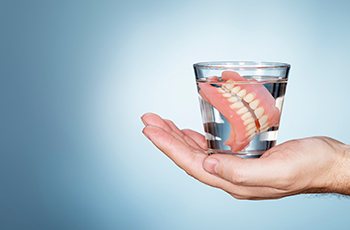 A hand holding a glass of liquid with a full set of dentures