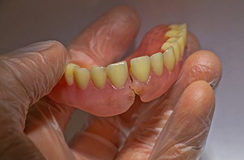 Closeup of a hand wearing a clear glove holding a fractured denture